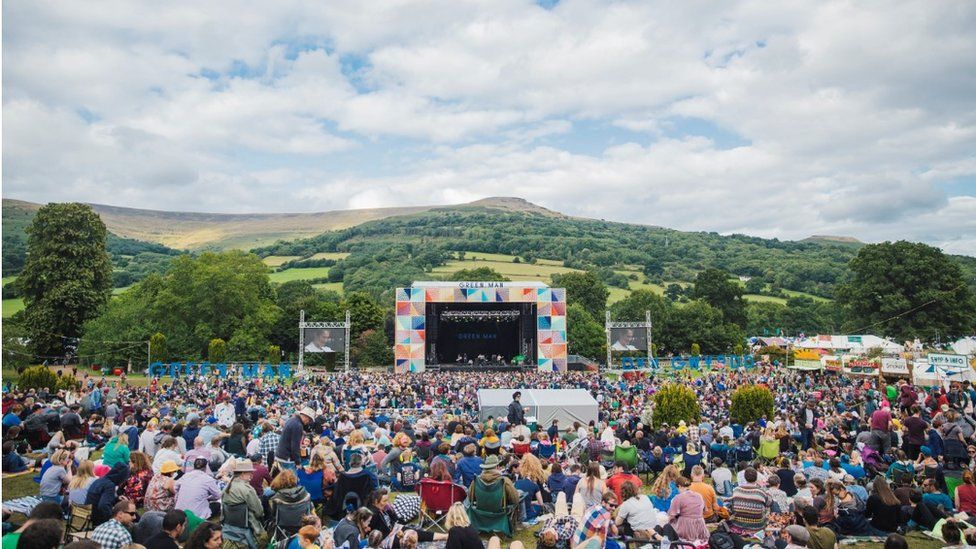 A large crowd gathers to watch the performers surrounded by a scenic landscape.