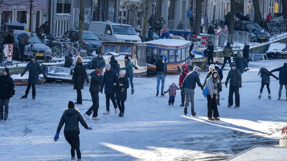 People walk and skate on ice on the Prinsengracht canal in Amsterdam, The Netherlands, 13 February 2021.