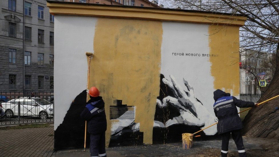 Municipal workers paint over a graffiti image of jailed Russian opposition politician Alexei Navalny