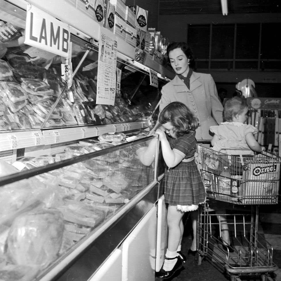 A mother and her two children shopping in a supermarket in the 1950s