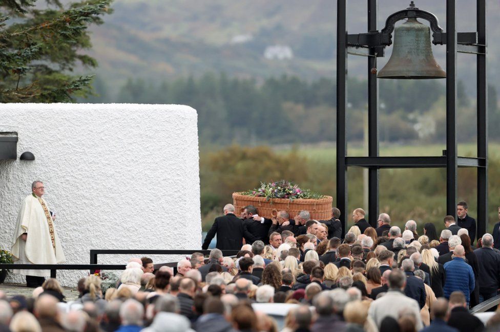 A priest watches as the coffin of Jessica Gallagher is carried towards St Michael's Church in Creeslough, with hundreds of mourners following