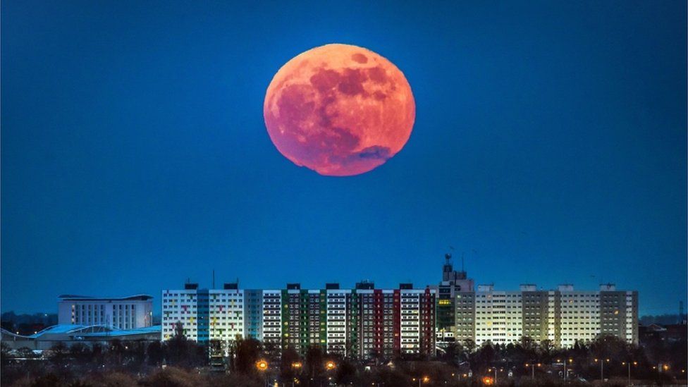 Moon, pictured large and reddish in tone, above Hull apartments in Yorkshire, UK