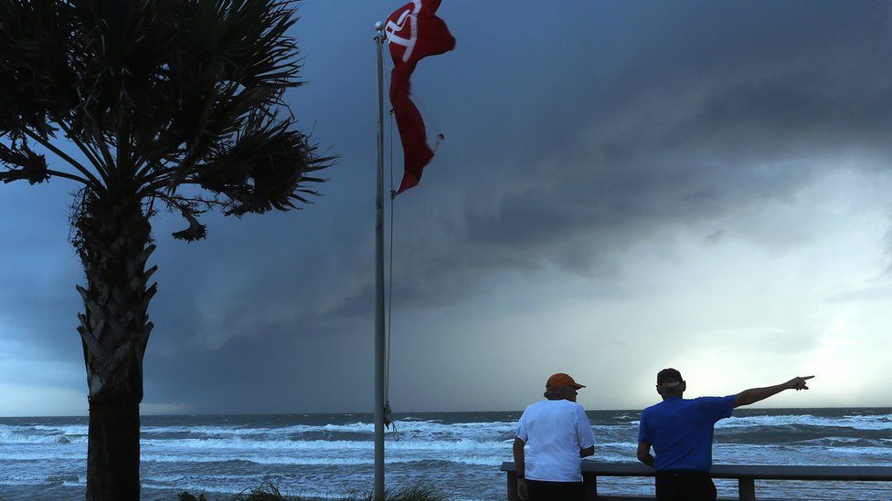 Two men stand looking out at the sea in Florida as the sky grows darker and more stormy