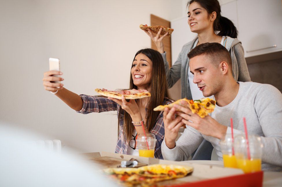 Young people photographing themselves eating pizza