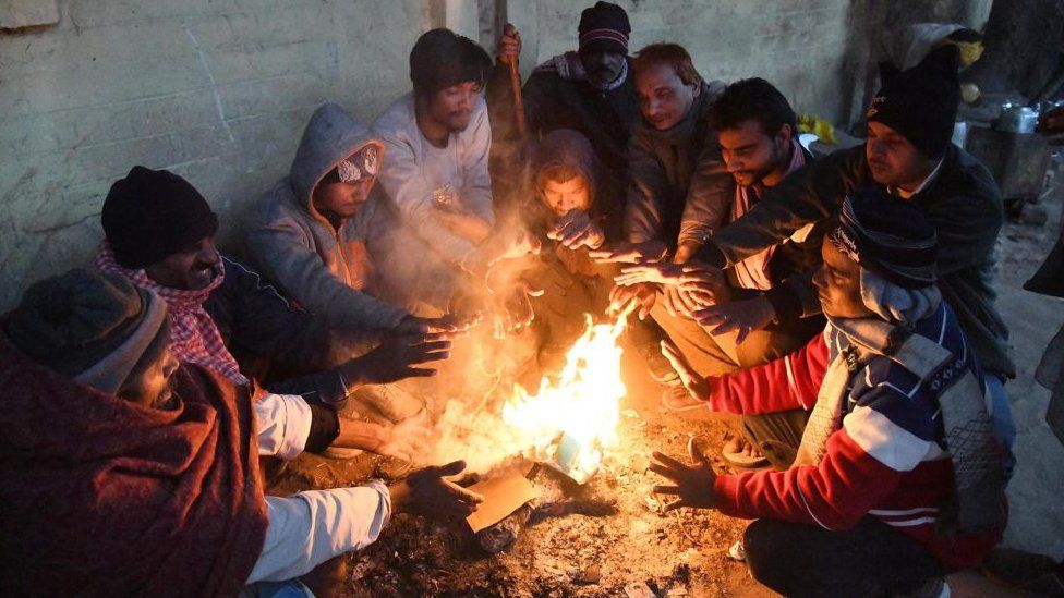 People sitting around bonfire to warm themselves during a cold winter evening on January 12, 2023 in New Delhi, India.