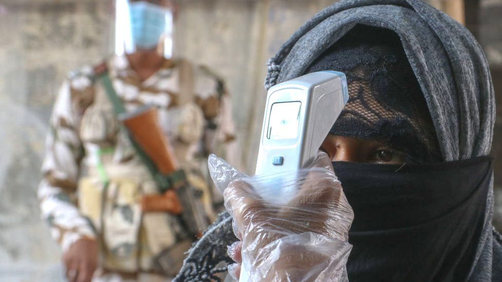 A security personal checks the body temperature of a woman wearing mask shows before her vote at polling station