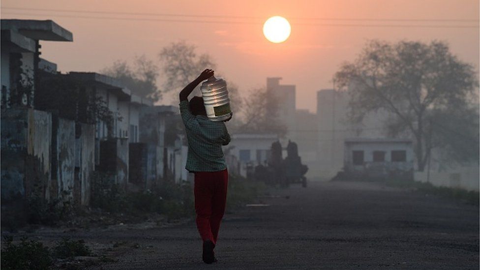 На этом снимке, сделанном 18 марта 2015 г., изображен рабочий-мигрант, несущий бутылку с водой, которую он наполнил из цистерны для воды в лагере, где он и другие, подобные ему, живут в районе Дварка, Нью-Дели, 18 марта 2015 г.