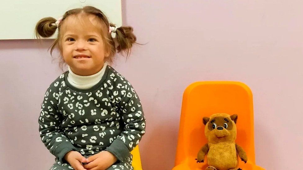 Liza sitting on a chair next to a teddy