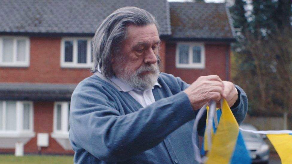 Ricky Tomlinson reprising his role as Brookside's Bobby Grant and can be seen putting up Ukrainian-themed bunting outside the character's family home ahead of Eurovision celebrations