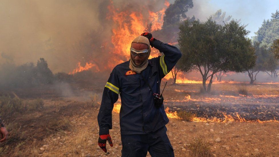 A firefighter walks next to rising flames as a wildfire burns near the village of Vati, on the island of Rhode