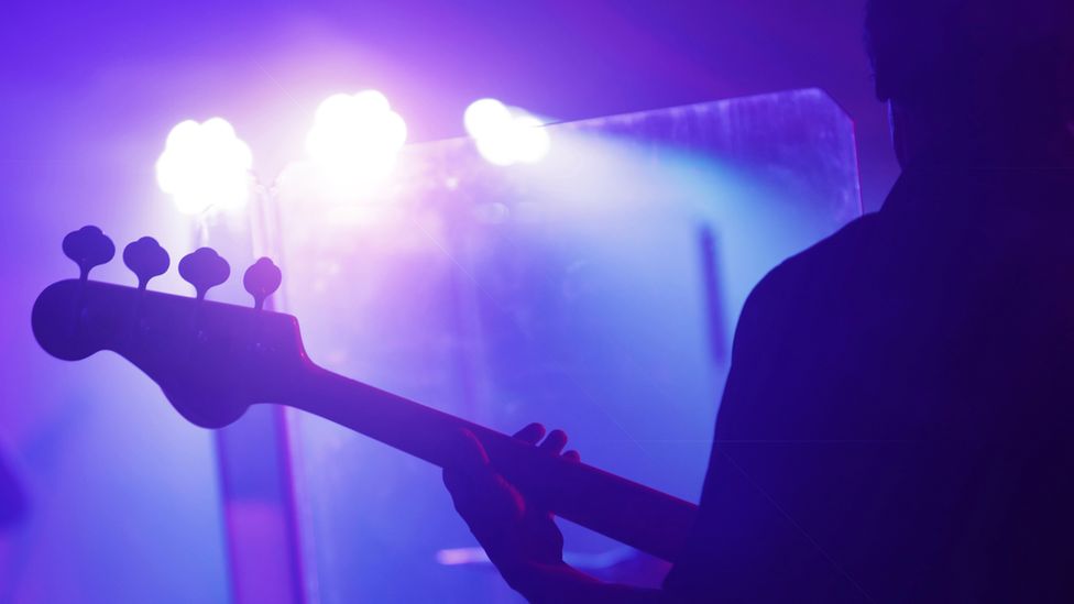 Силуэт человека, играющего на гитаре в ярко-фиолетовом свете сцены