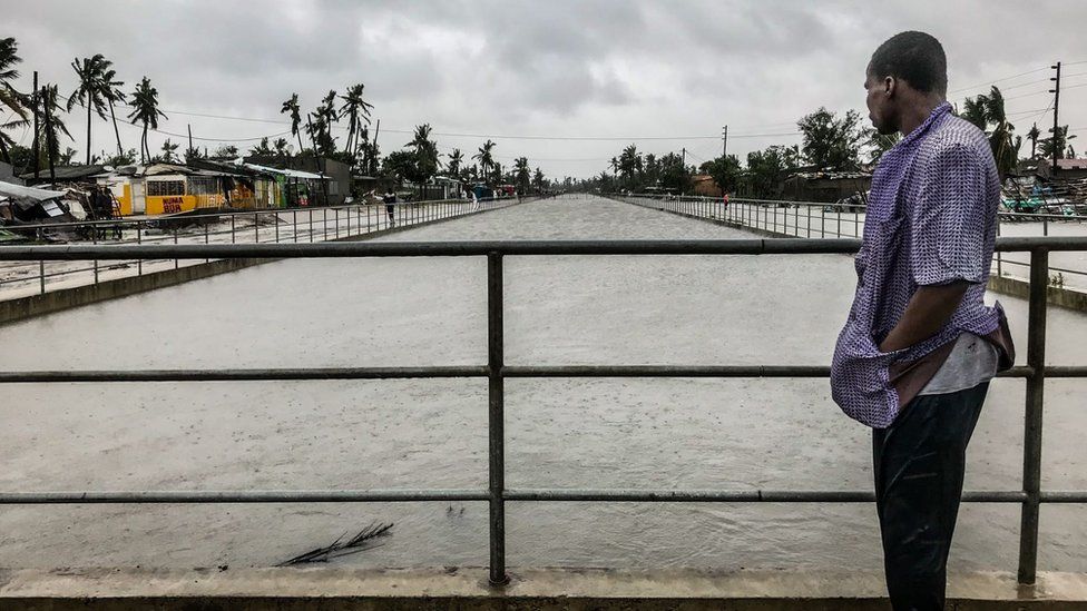 A man stands on a bridge overlooking a flooded river