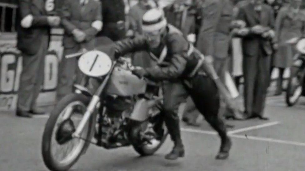 Old image of man pushing motorbike at start of race
