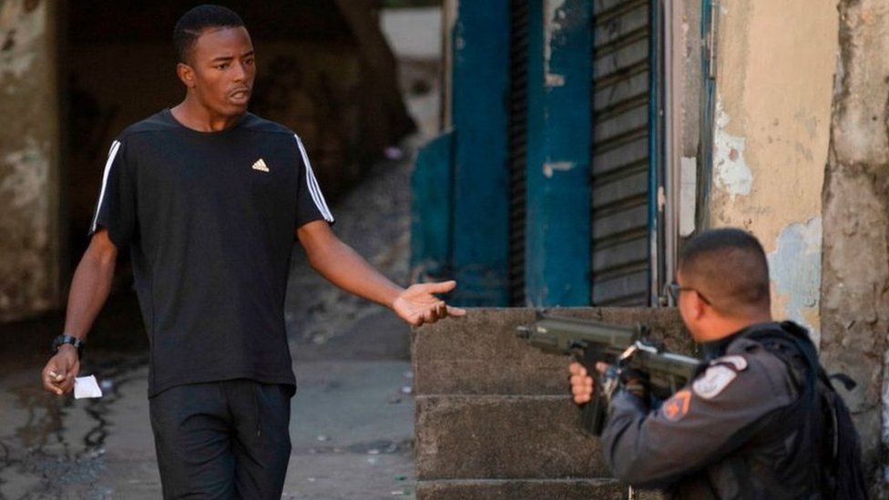 A police officer aims his weapon at a man after riots during a protest in Rio de Janeiro on 9 August 2019