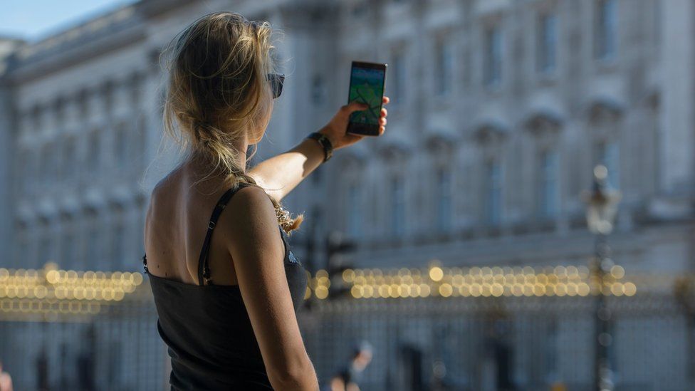 A woman is seen playing Pokémon Go on her phone next to Buckingham Palace in London