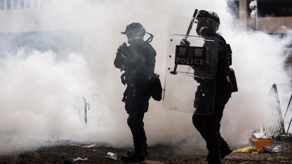 Police officers surrounded by tear gas during a rally by protesters against a controversial extradition law proposal, in Hong Kong on 12 June 2019