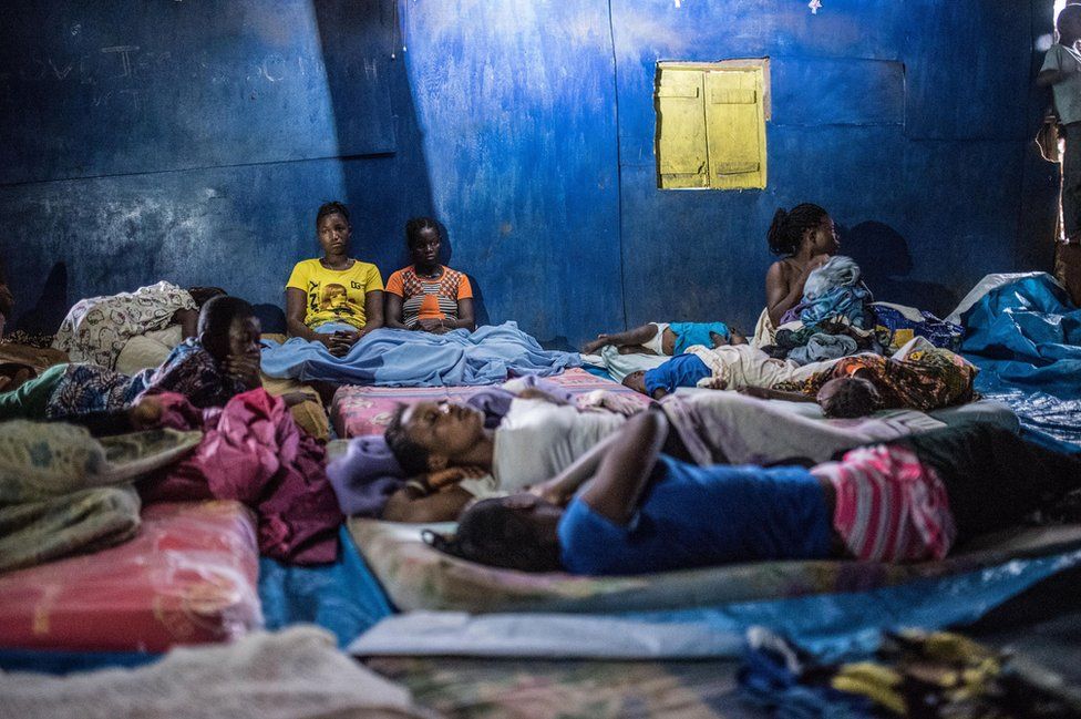 Women and children sleep on the floor of a church built from corrugated iron