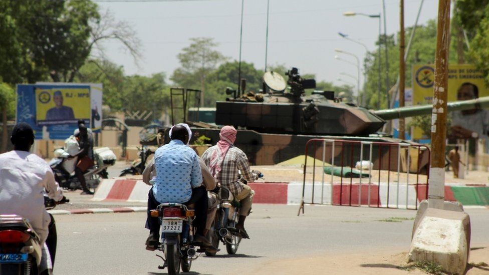 People riding on motorbikes past a tank near the presidential palace in N'Djamena, Chad
