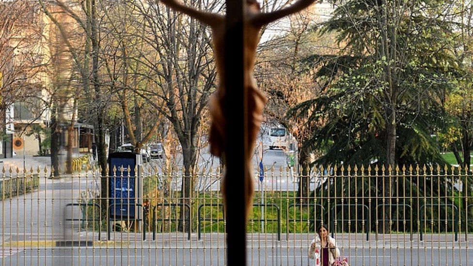 A woman follows from outside the Good Friday prayer at the Saint Peter Cathedral, in Tirana