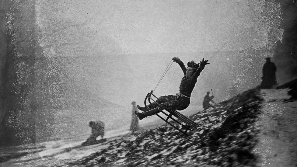 30th January 1937: A young woman leaps into the air on a toboggan as she speeds down snow-covered Hampstead Heath