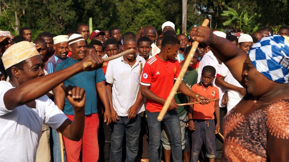 Men and women line up and take turns to 'fight' with batons while a band plays folk music