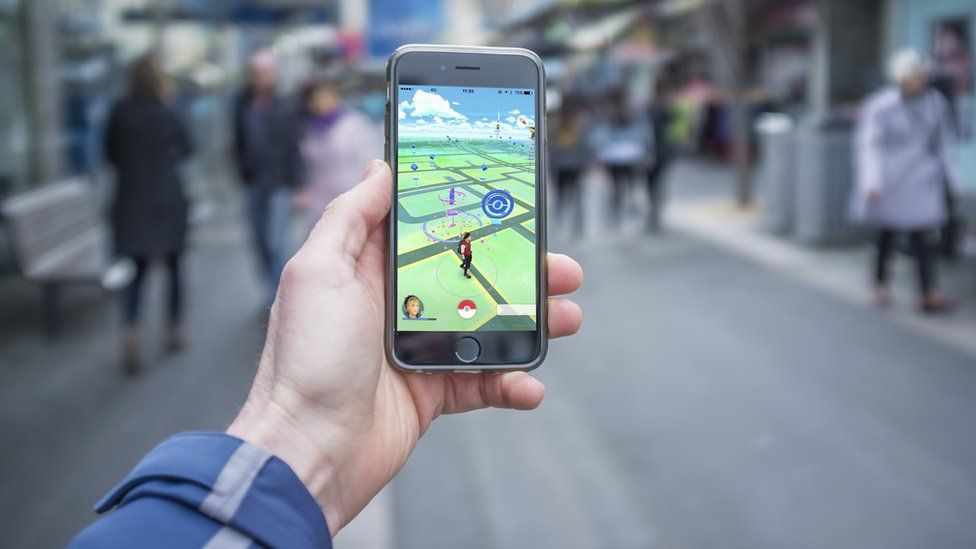 Male hand holding iPhone 6 with Pokemon Go game on a busy street