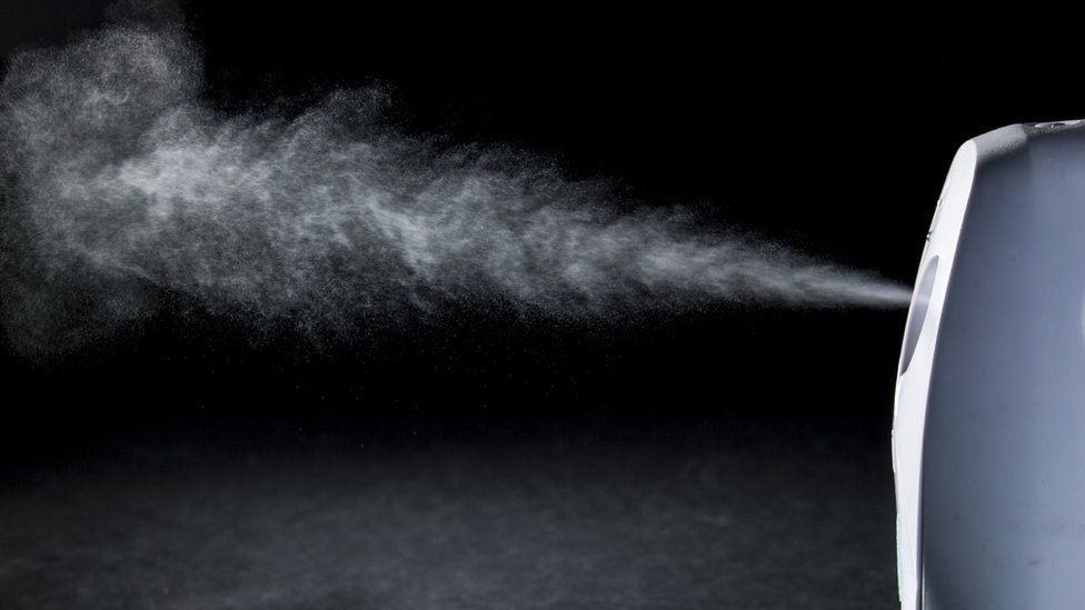 Plug-in air freshener spraying mist onto a black background