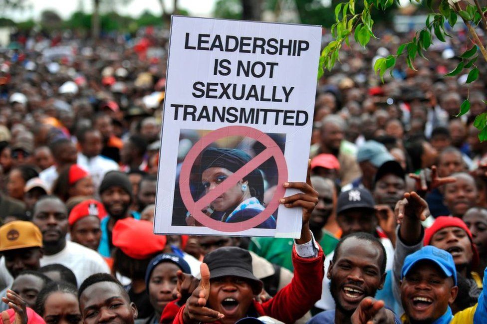 Anti-Mugabe protesters in Zimbabwe mass in Harare, one of whom holds a signs which reads 'leadership is not sexually transmitted'.