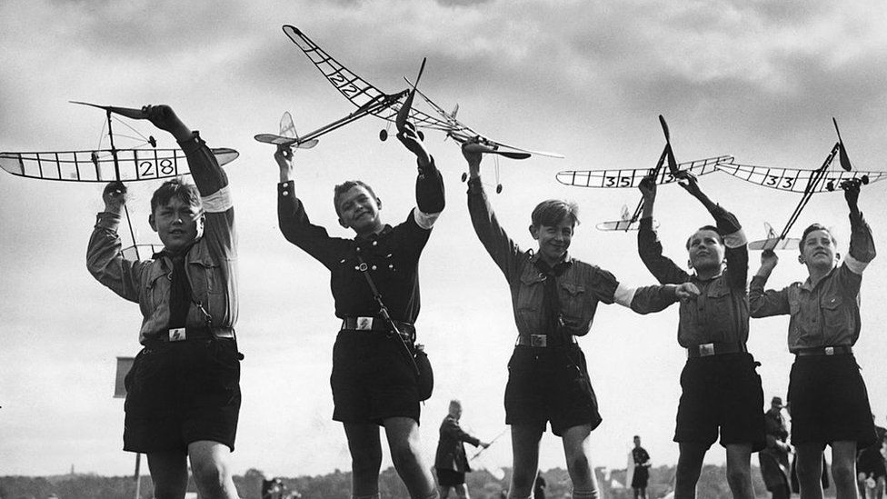 Niños alemanes con uniformes de la Juventud Hitleriana jugando con aviones de juguete.