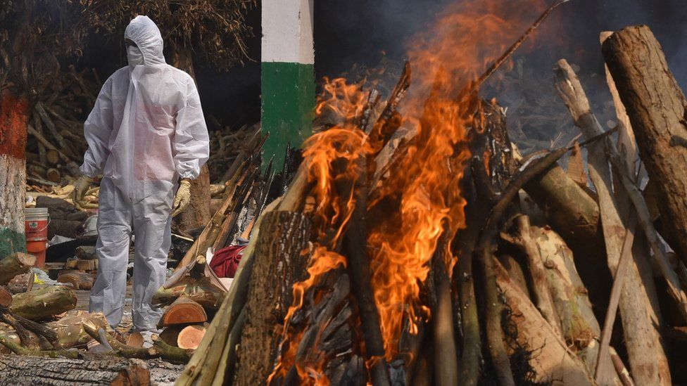 A Family member, wearing a Personal Protective Equipment (PPE), performs the last rites for COVID-19 victims at a cremation ground in Delhi, India, 29 April 2021.