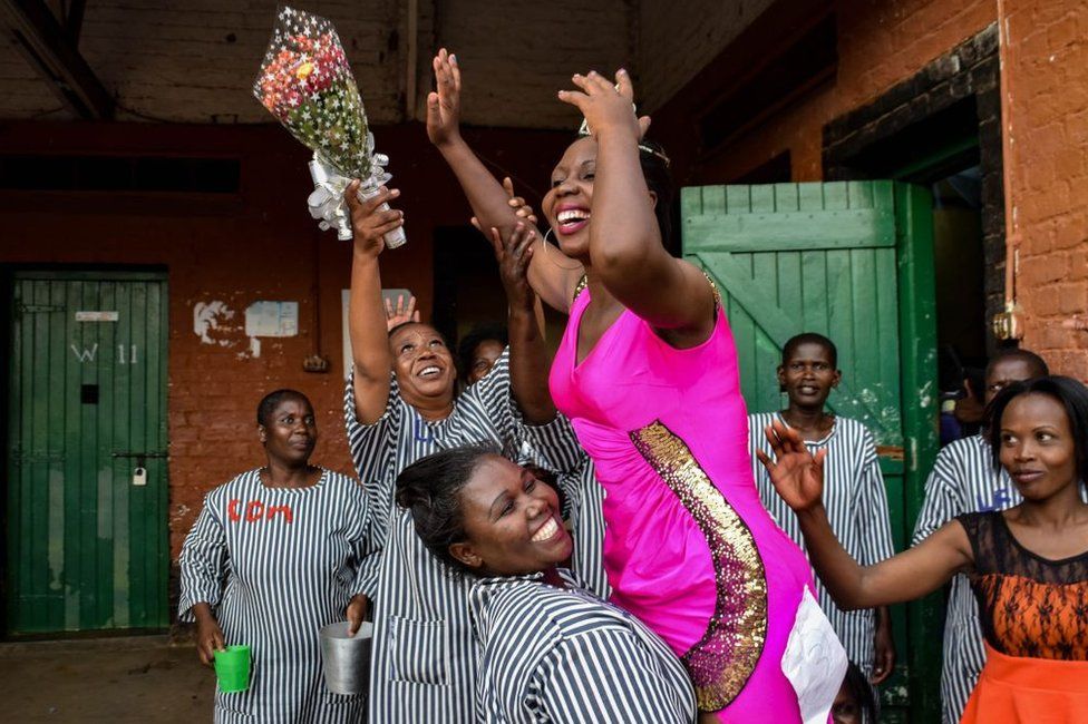 Inmates at Kodiaga Womens Prison celebrate with the newly selected Miss Kodiaga Womens Prison 2019, who is wearing a bright pink dress with glitter on one side, as well as a tiara, in Kisumu, Kenya - Saturday 17 February 2019