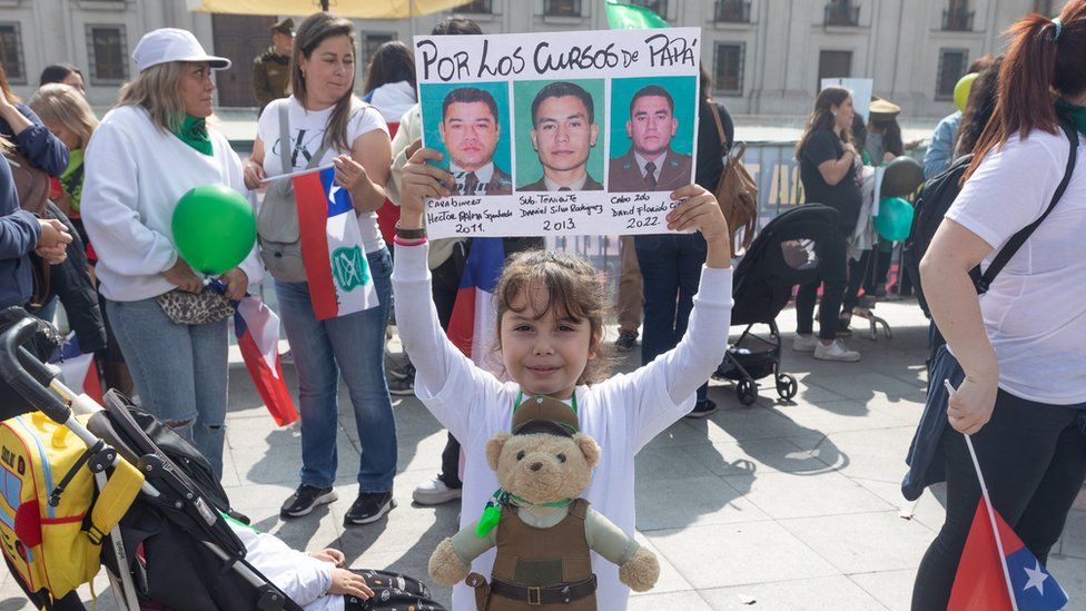 Дочь чилийского полицейского держит транспарант с фотографиями чилийских полицейских, погибших при исполнении служебных обязанностей, во время марша, организованного семьями чилийских полицейских, погибших при исполнении служебных обязанностей, в Сантьяго, Чили, 16 апреля.