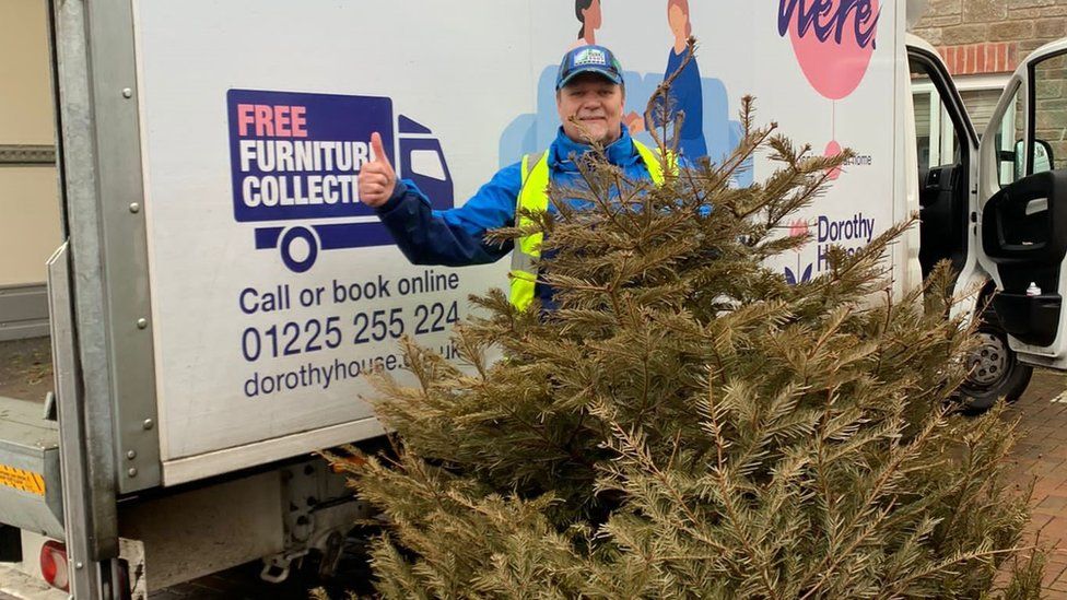 Volunteer in front of a large van with a Christmas tree