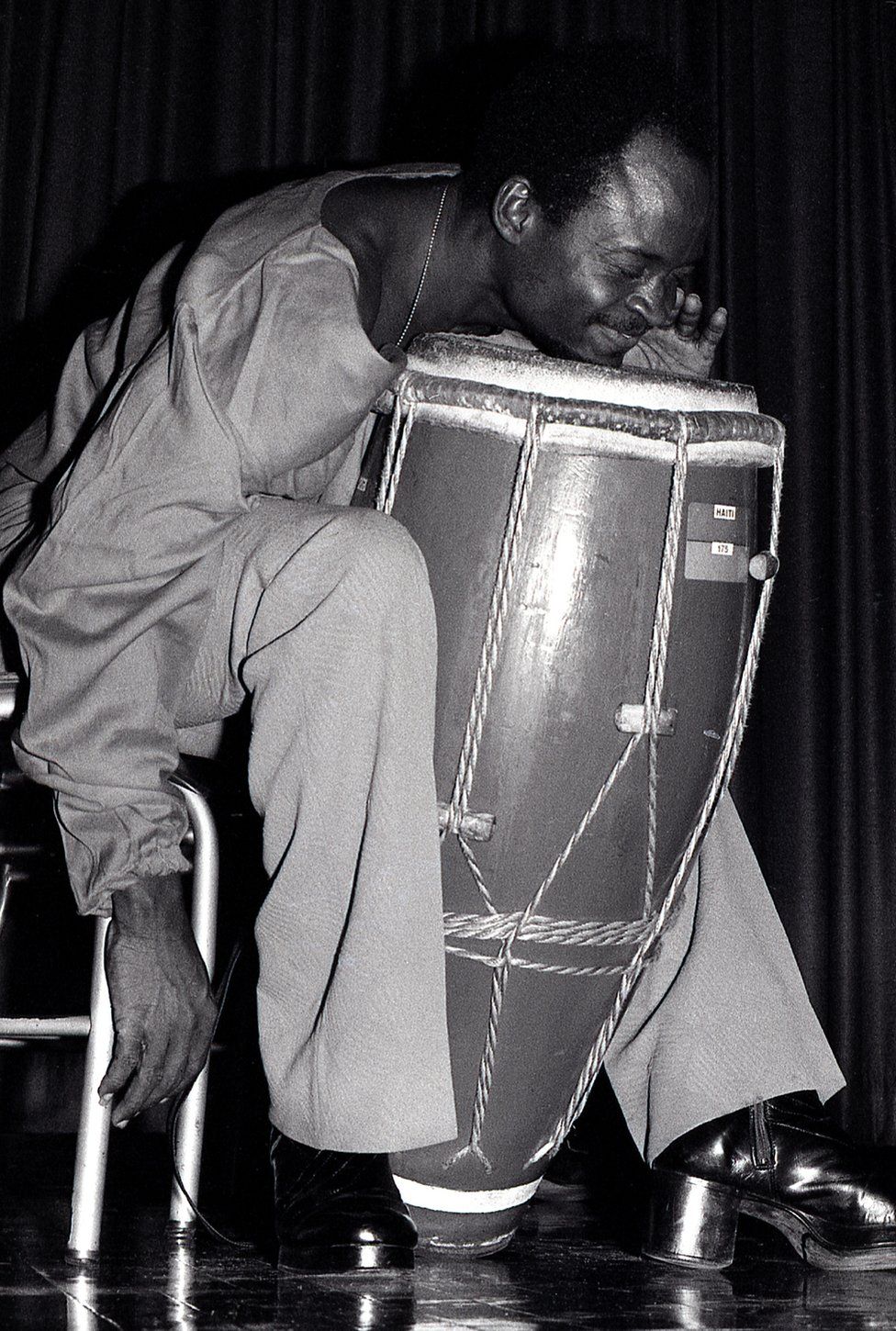 A man leans his chin onto a drum as he plays it, he is elated
