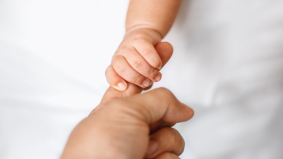 Новорожденный ребенок держит палец взрослого