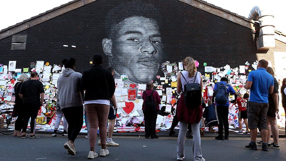 People look at the newly repaired mural of England footballer Marcus Rashford, which is displayed on the wall of a cafe on Copson Street, Withington, on 14 July 2021