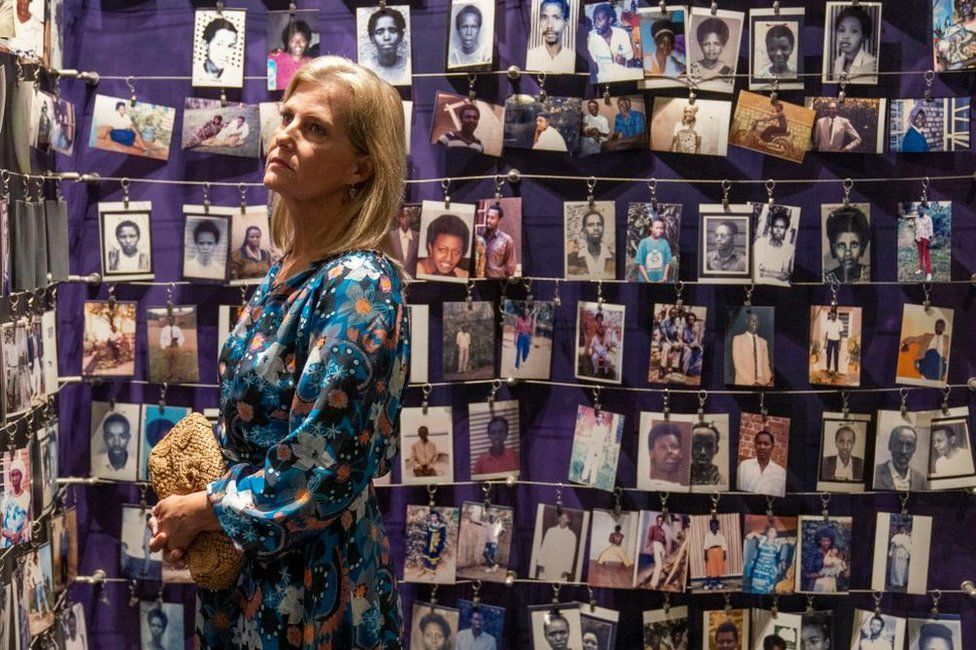 The Countess of Wessex with a sombre expression looking at several photos of victims of the Rwandan genocide mounted on the wall.