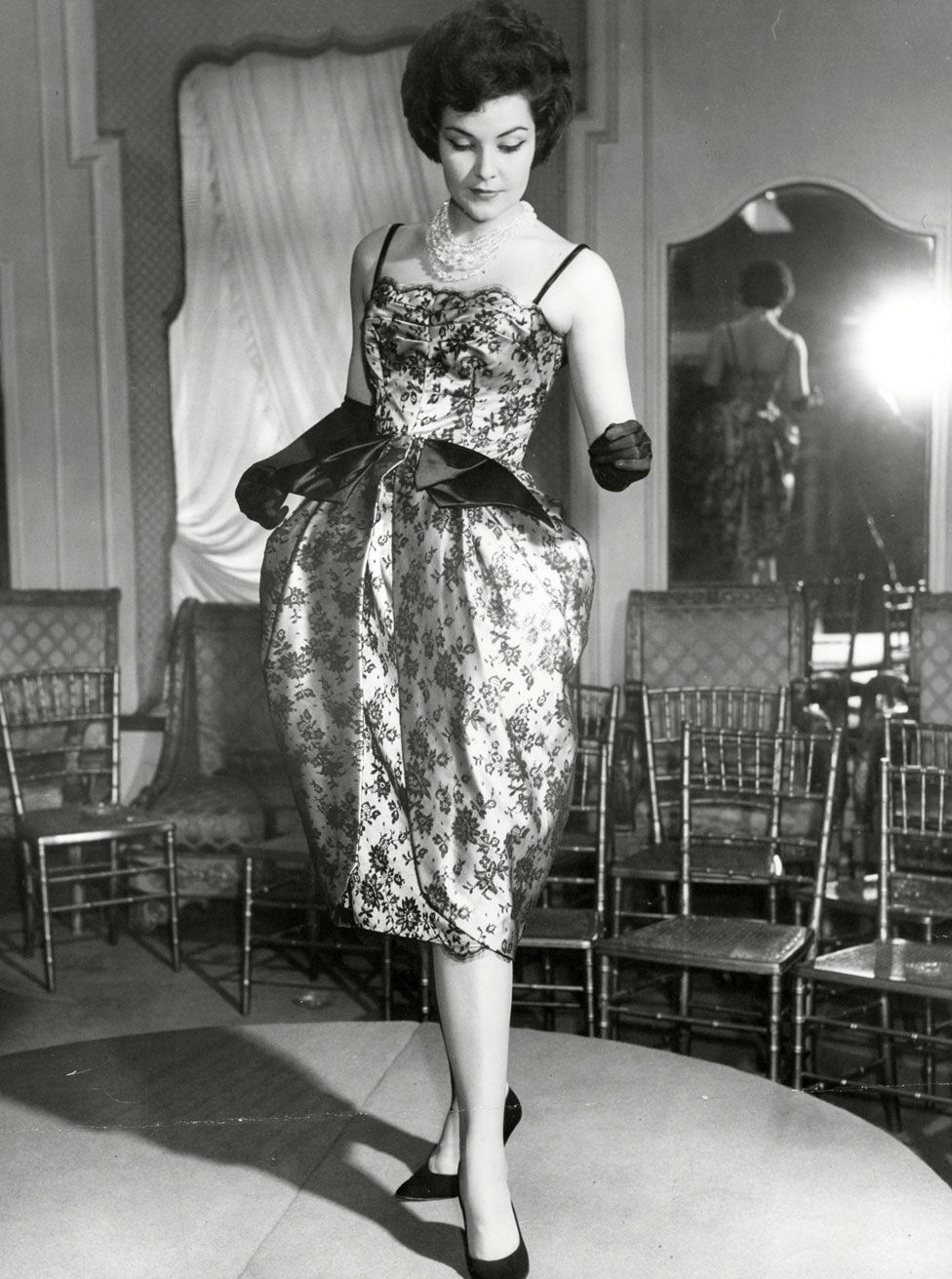 A model stands on a stage wearing a satin dress