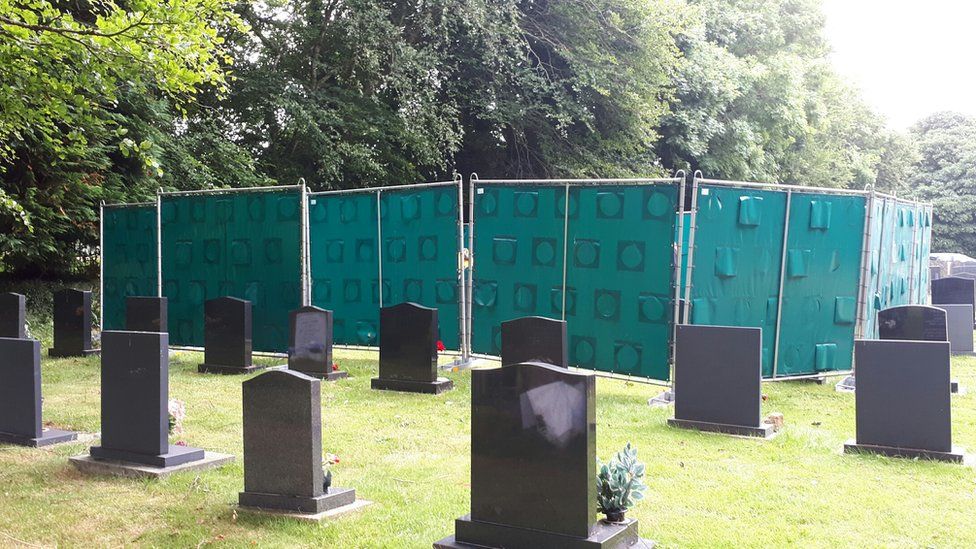 Large screens in a graveyard - hiding the exhumation process