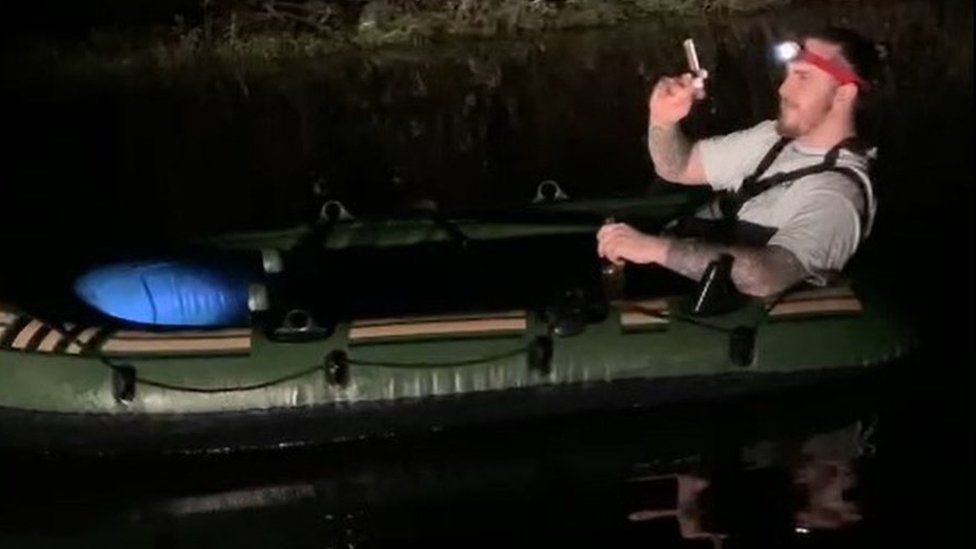 Man reclining in a dinghy in the dark smoking a cigar and wearing a head torch