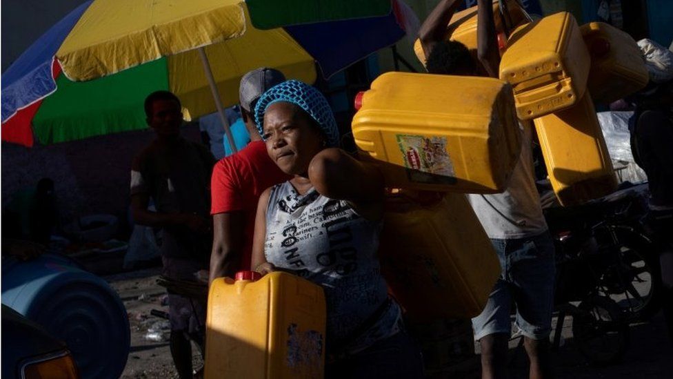 Местные жители несут контейнеры, использованные для нефти и бензина, во время нехватки топлива в Порт-о-Пренсе, Гаити, 24 октября 2021 г.