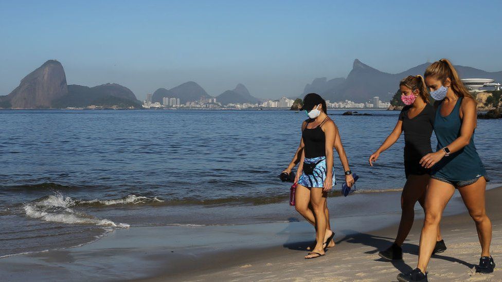 People walk wearing a protective mask on Icarai beach, as the Sugarloaf Mountain is seen in the distance, during the coronavirus (COVID-19) pandemic on May 21, 2020 in Niteroi, Brazil