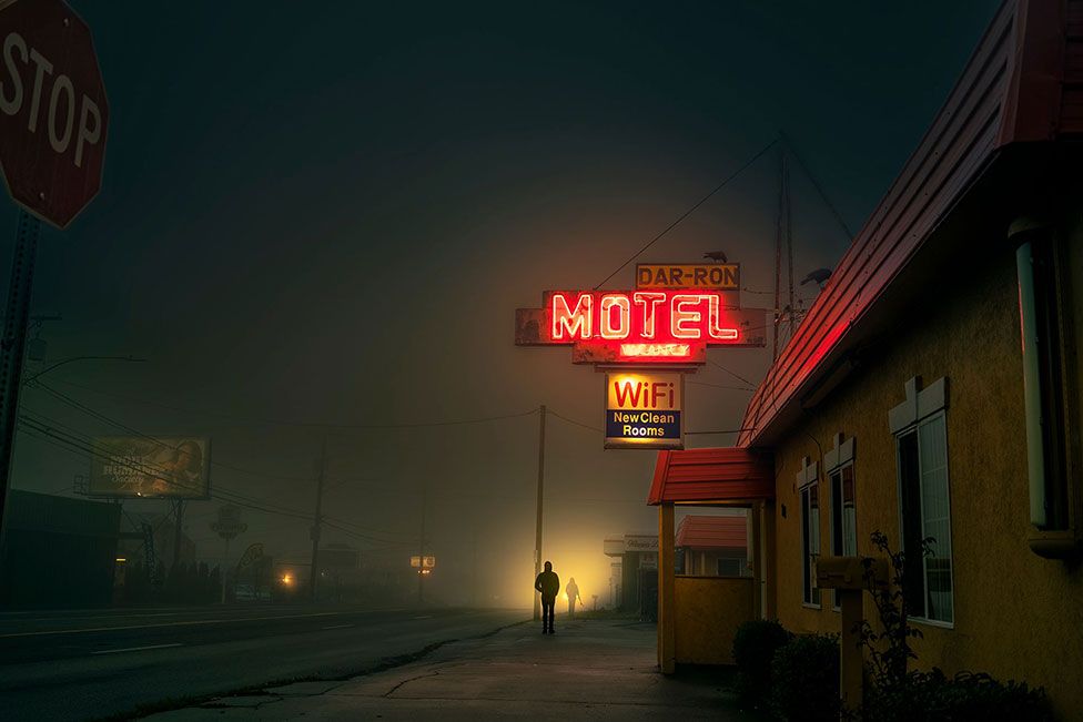 A view of a misty street at night with neon motel sign