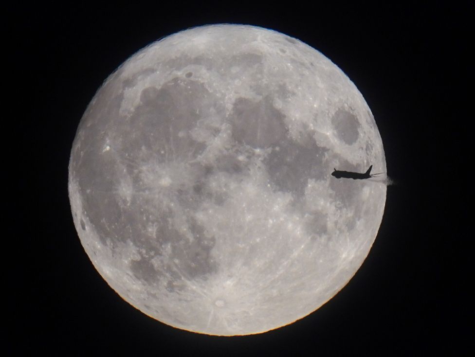 A plane is seen with the full moon behind
