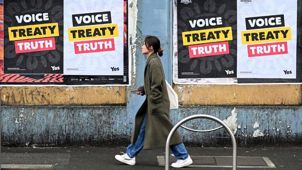 A woman walks past posters advocating for an Aboriginal voice and treaty