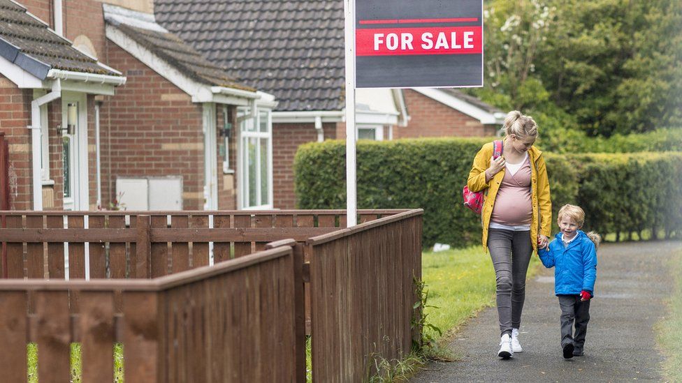 Pregnant woman and son walking past a for sale sign