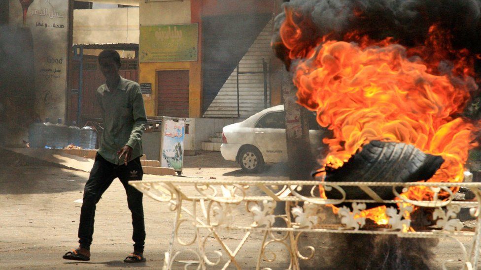 A Sudanese protester walks past a burning tyre near Khartoum's army headquarters