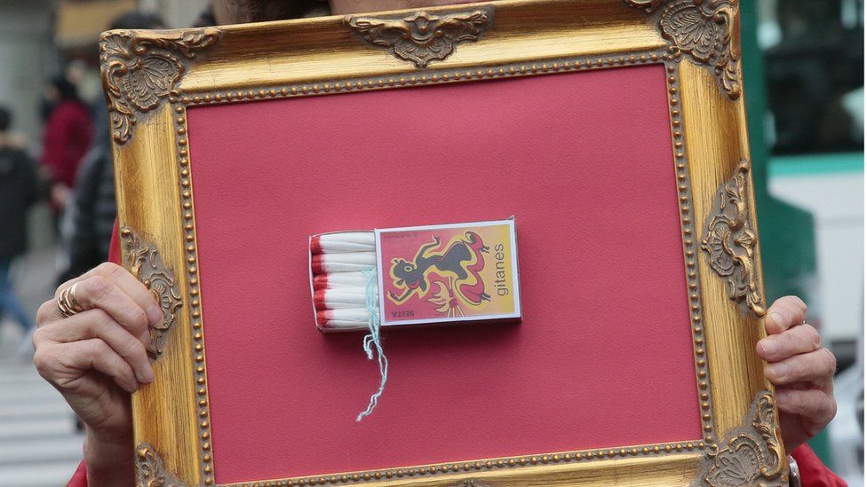 A woman holds a frame with a 'Gitanes' matchbox full of tampons during a demonstration in Paris on November 11, 2015, calling for reduced taxes on tampons and women's sanitary products.