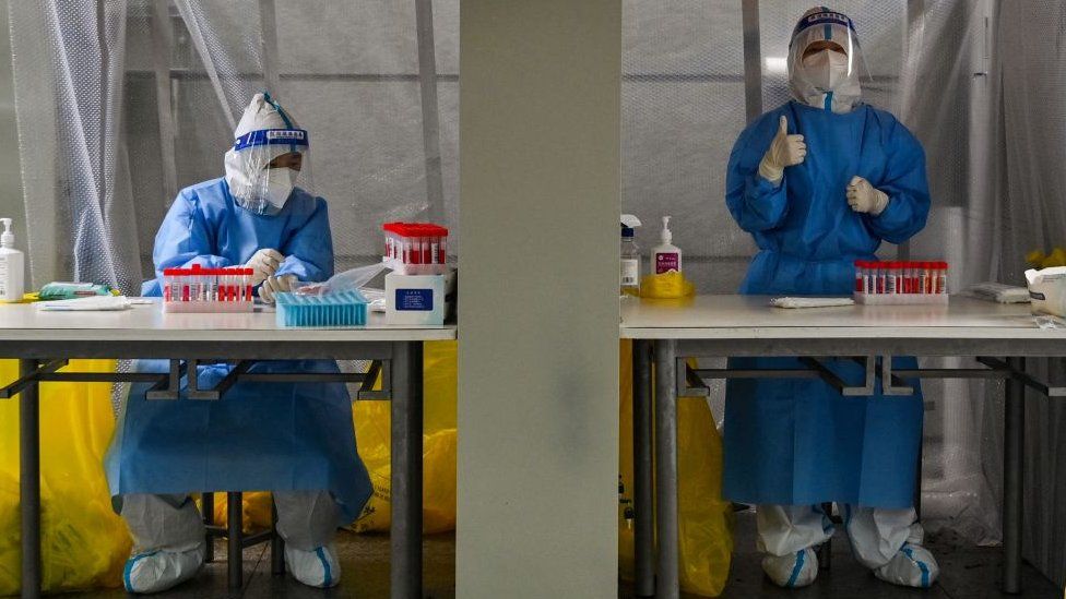 Health workers wearing personal protective equipment wait to take swab samples from people during a Covid-19 coronavirus lockdown in the Xuhui district of Shanghai.
