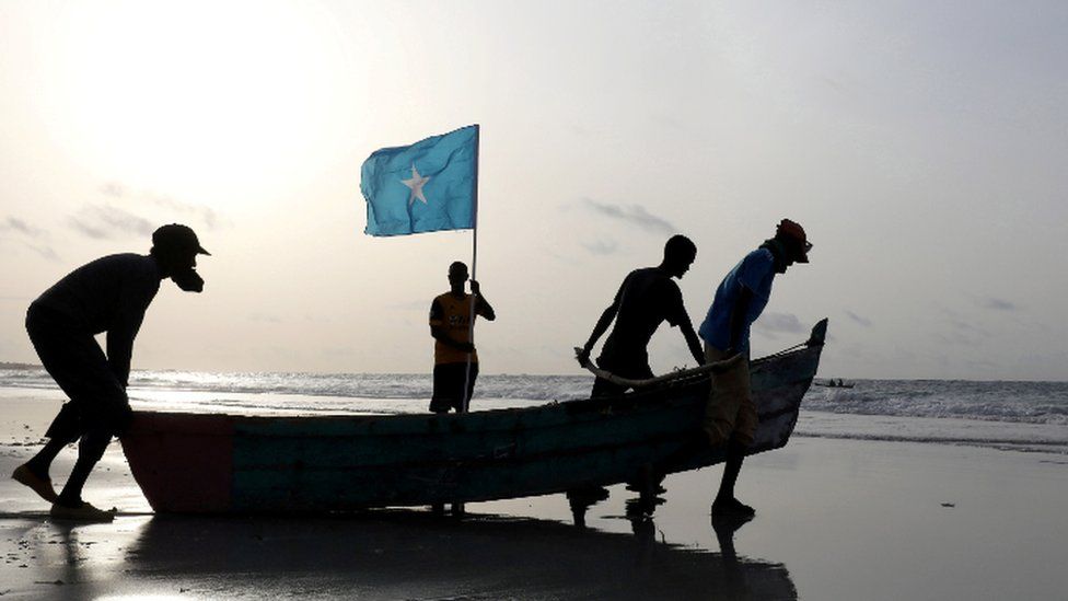 Fishermen carry a boat in to the water on Lido Beach, Mogadishu, Somalia - Friday 18 June 2021